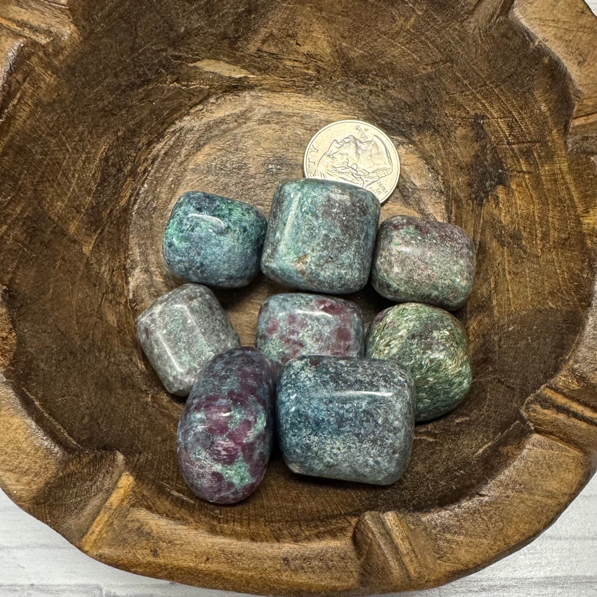 Wooden bowl with polished stones and a coin for scale on a wooden surface.