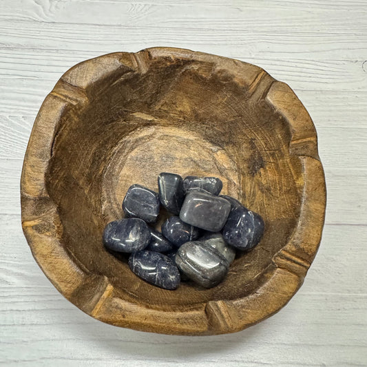 Wooden bowl with dark stones on a light wooden surface