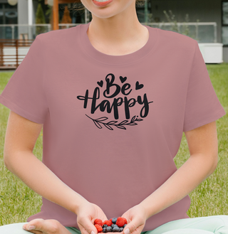 Mauve Be Happy t-shirt with hand-lettered script, hearts, and a leaf design, worn outdoors while holding berries