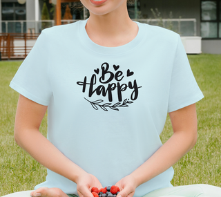 Heather Prism Ice Blue Be Happy t-shirt with hand-lettered script, hearts, and a leaf design, worn sitting outdoors