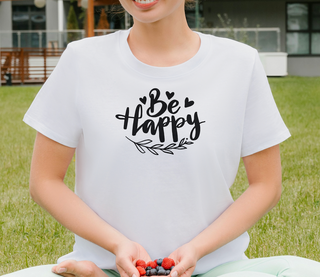 Ash Be Happy t-shirt with hand-lettered script, hearts, and a leaf design, worn in a garden