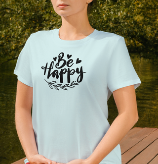 Heather Prism Ice Blue Be Happy t-shirt with hand-lettered script, hearts, and a leaf design, worn standing outdoors
