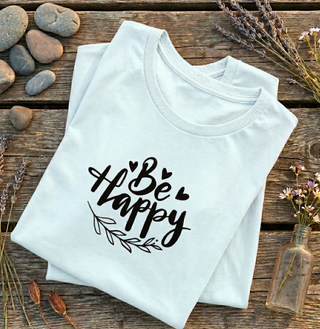 Folded Heather Prism Ice Blue Be Happy t-shirt with hand-lettered script, hearts, and a leaf design on a wooden surface with stones and flowers