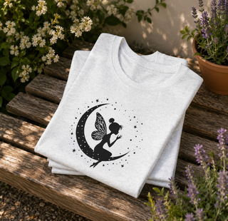 Folded Ash Fairy on Crescent Moon t-shirt with a black fairy and stars design on a wooden surface with plants