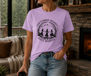 Heather Prism Lilac God Forbid Women Have Hobbies t-shirt with a vintage moonlit forest design of two women dancing, worn in a cozy living room