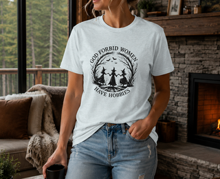 White God Forbid Women Have Hobbies t-shirt with a vintage moonlit forest design of two women dancing, worn in a cozy living room
