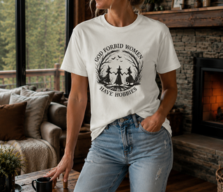 White God Forbid Women Have Hobbies t-shirt with a vintage moonlit forest design of two women dancing, worn in a cozy living room