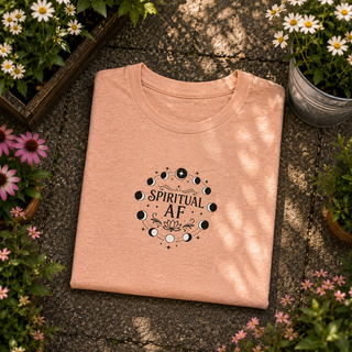 Folded Heather Peach Spiritual AF moon phase tee on a stone surface with flowers