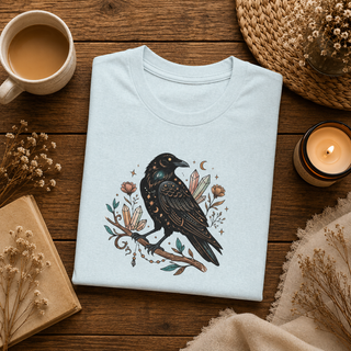 Folded Crow Moon tee featuring a hand-drawn crow with crescent moons and florals, styled in a flatlay