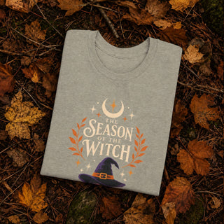 Heather stone unisex cotton tee printed with a witch hat, crescent moon, stars, and orange laurel leaves beneath 'The Season of the Witch' lettering.