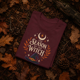 Maroon unisex cotton tee printed with a witch hat, crescent moon, stars, and orange laurel leaves beneath 'The Season of the Witch' lettering.