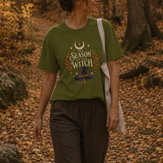 Cotton tee printed with a witch hat, crescent moon, stars, and orange laurel leaves beneath 'The Season of the Witch' lettering.