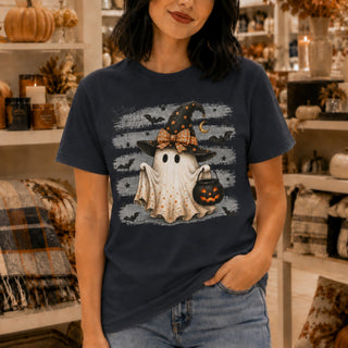 A woman wearing a navy blue graphic t-shirt with a cute Halloween ghost design, standing in a cozy, warmly lit retail store.
