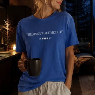 A woman wearing a royal blue graphic t-shirt with the text 'THE MOON MADE ME DO IT.' and moon phase symbols printed in white.