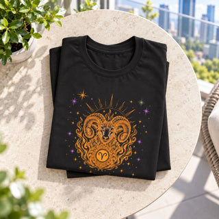 A folded black t-shirt with a detailed golden ram and sun graphic, displayed on a round stone table with a city skyline background.