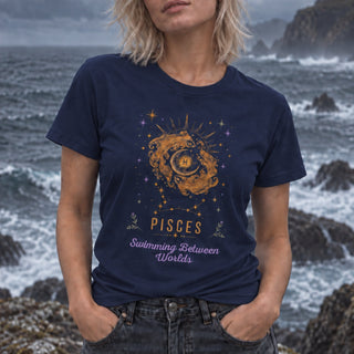 A woman wearing a navy blue graphic t-shirt with a Pisces zodiac design, standing against a rocky, ocean-coastal background.