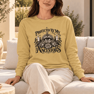 A woman wearing a pale yellow long-sleeve graphic sweatshirt and cream pants, sitting on a light-colored sofa in a bright, modern living room setting.