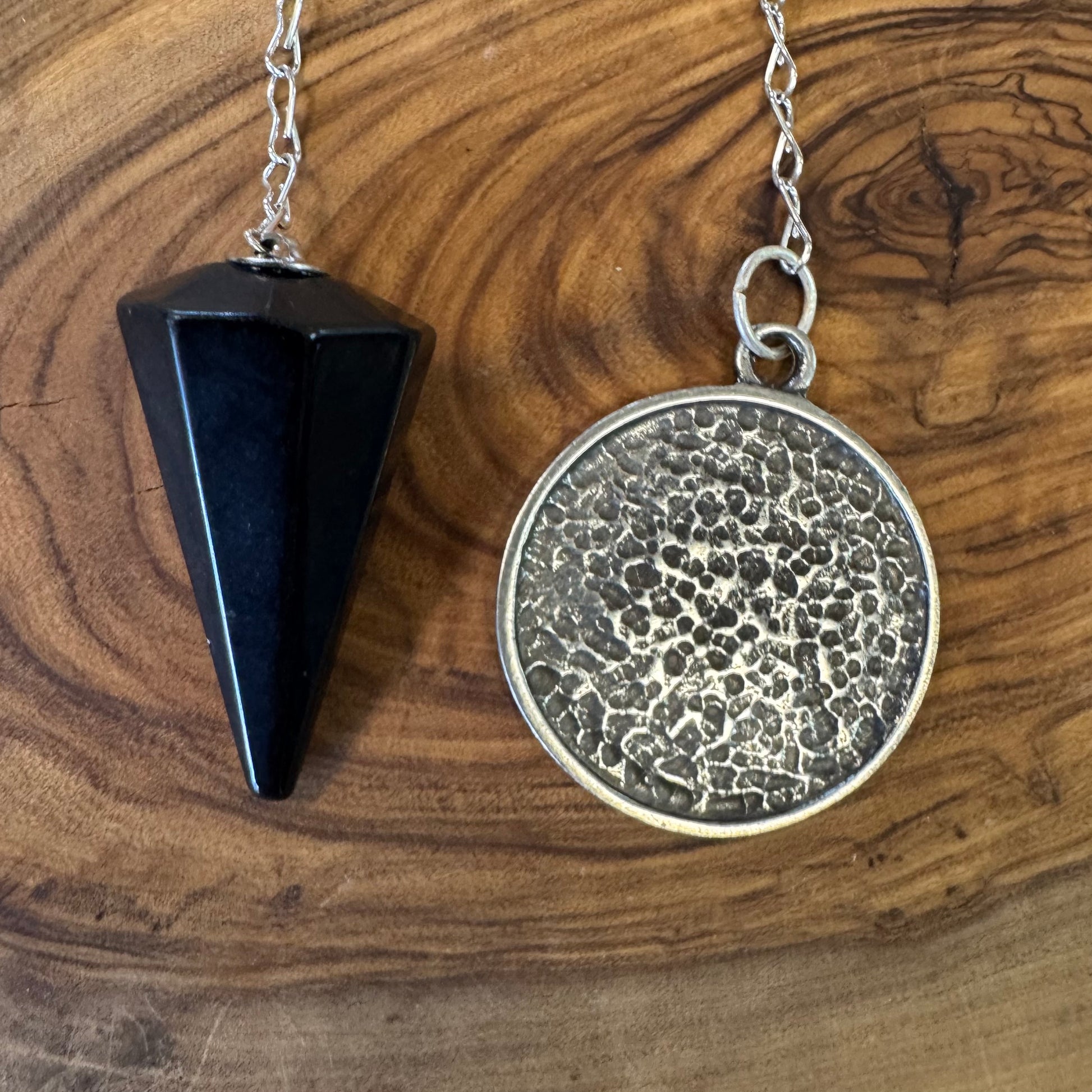 Black obsidian pyramid-shaped pendant and silver circular pendant on a wooden surface