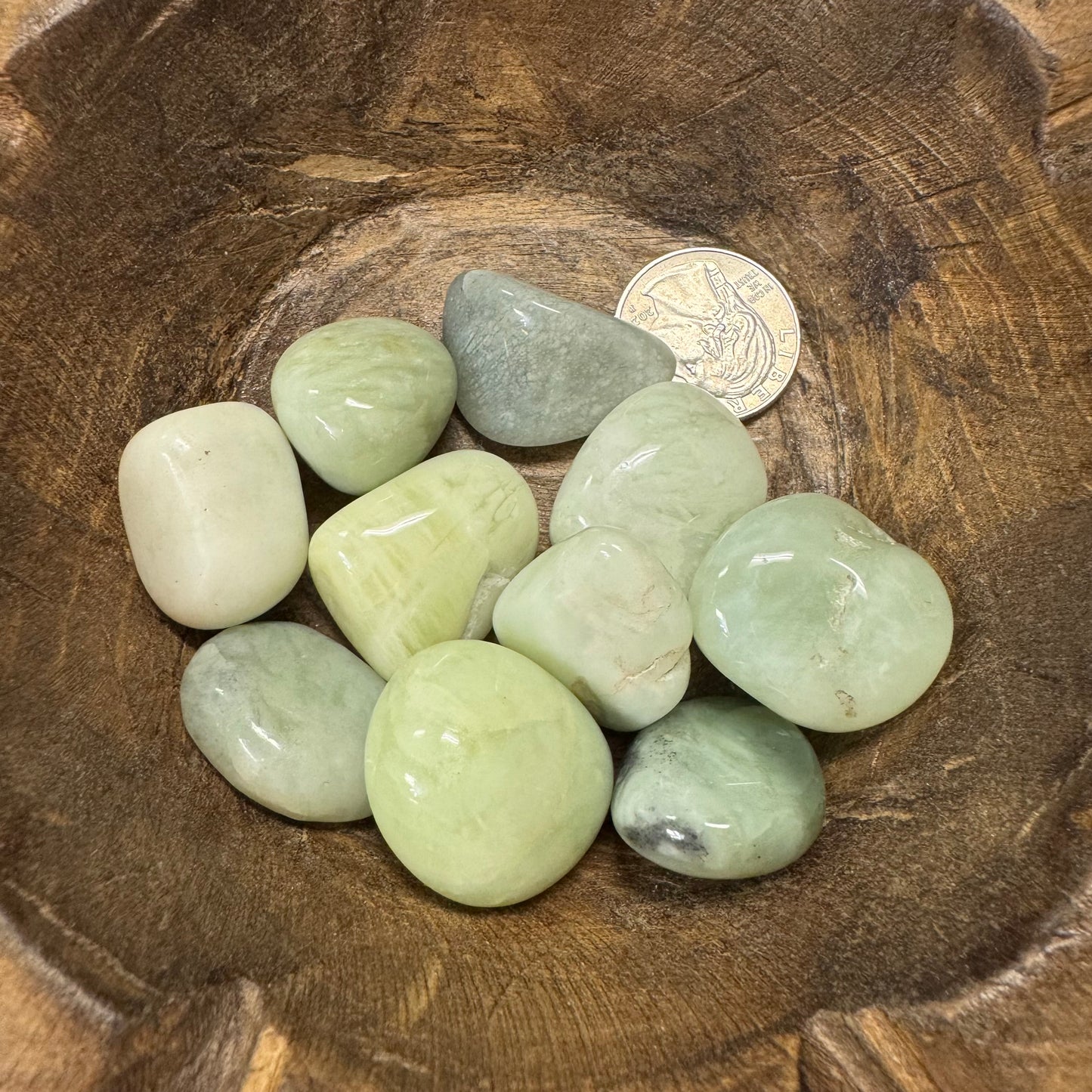 Green stones in a wooden bowl with a coin for scale