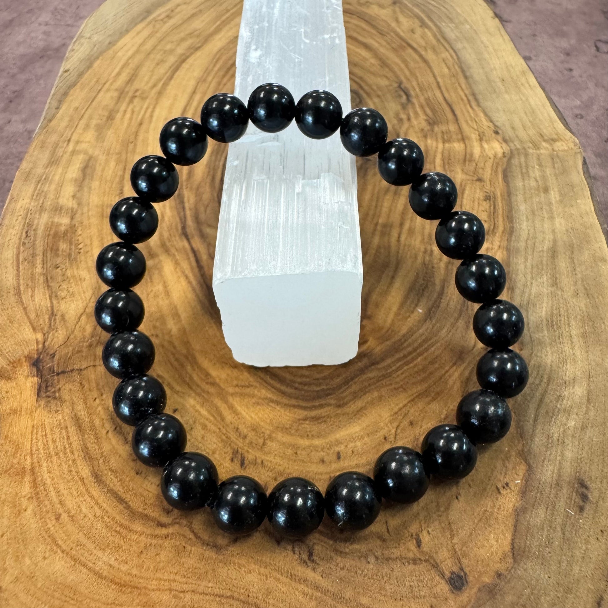 Black beaded bracelet on a wooden surface with a crystal in the background