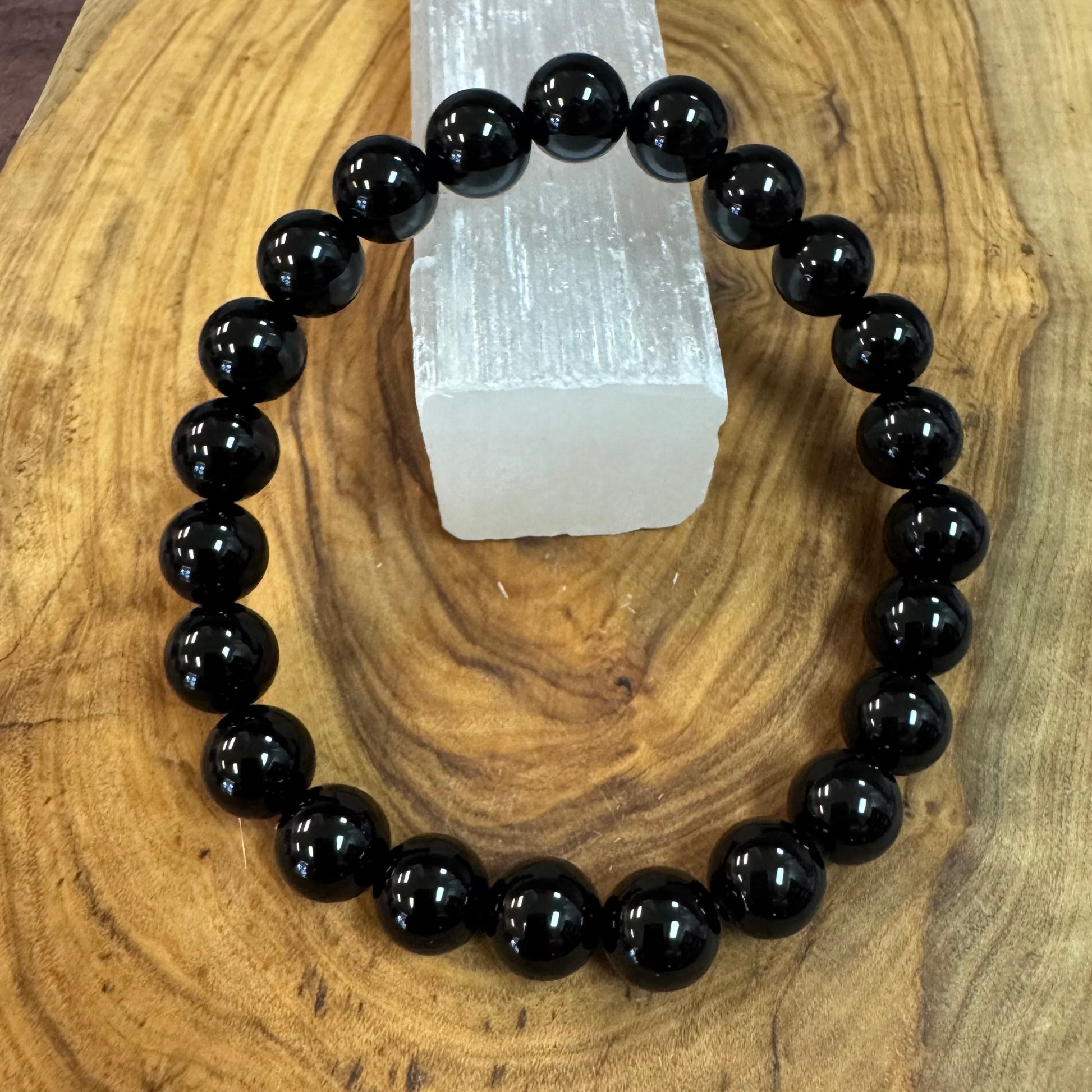Black beaded bracelet on a wooden surface with a crystal in the background
