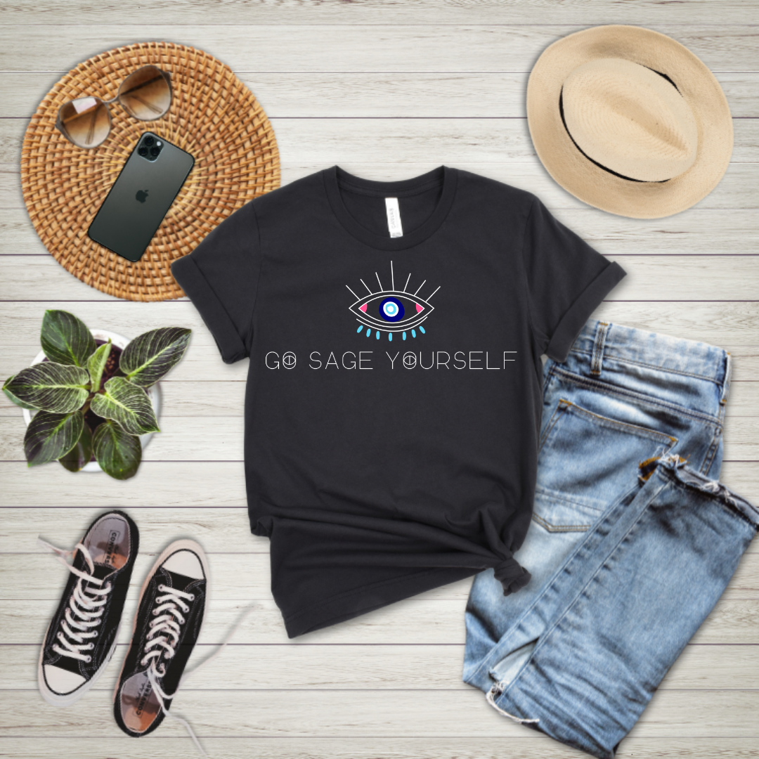 A black unisex crew neck t-shirt with a graphic that reads 'GO SAGE YOURSELF' on the front, displayed flat with a smartphone, sunglasses, a plant, and denim jeans around it.