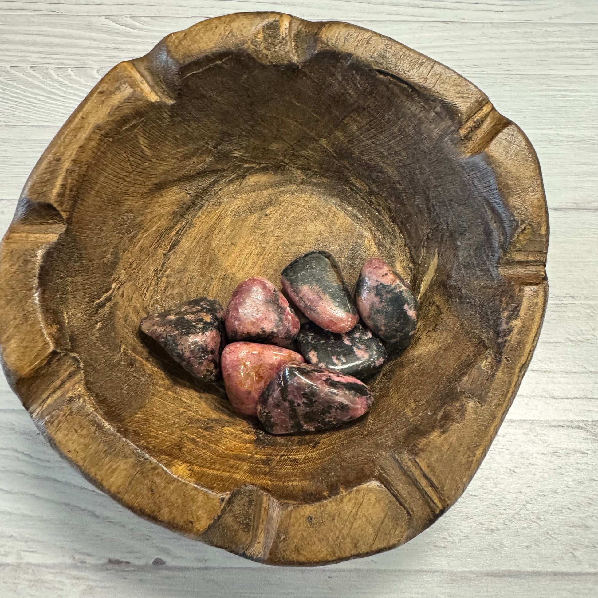 Wooden bowl with pink stones on a light wooden surface