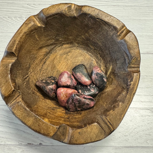 Wooden bowl with pink stones on a light wooden surface