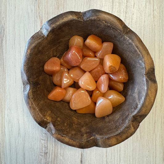 A collection of peach colored tumbled aventurine stones displayed in a wooden bowl.