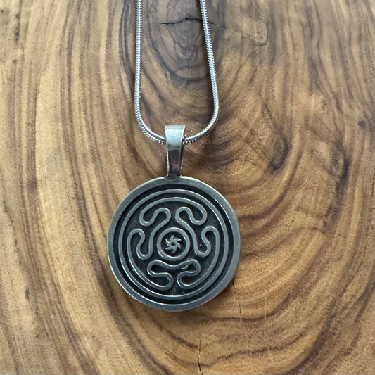 Silver labyrinth pendant necklace on a wooden surface Hecate