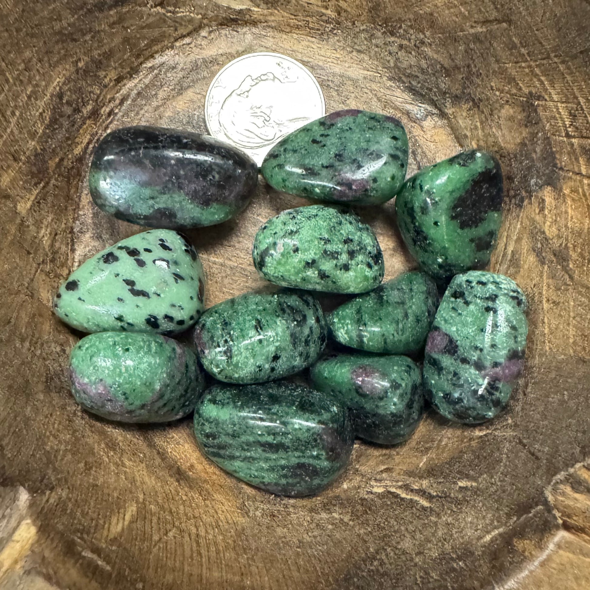 Green tumbled stones on a wooden surface with a coin for scale