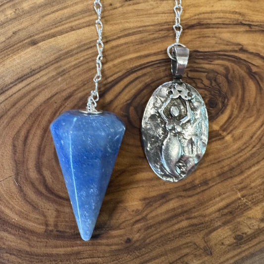 Blue crystal pendulum and silver ornate pendant on a wooden surface