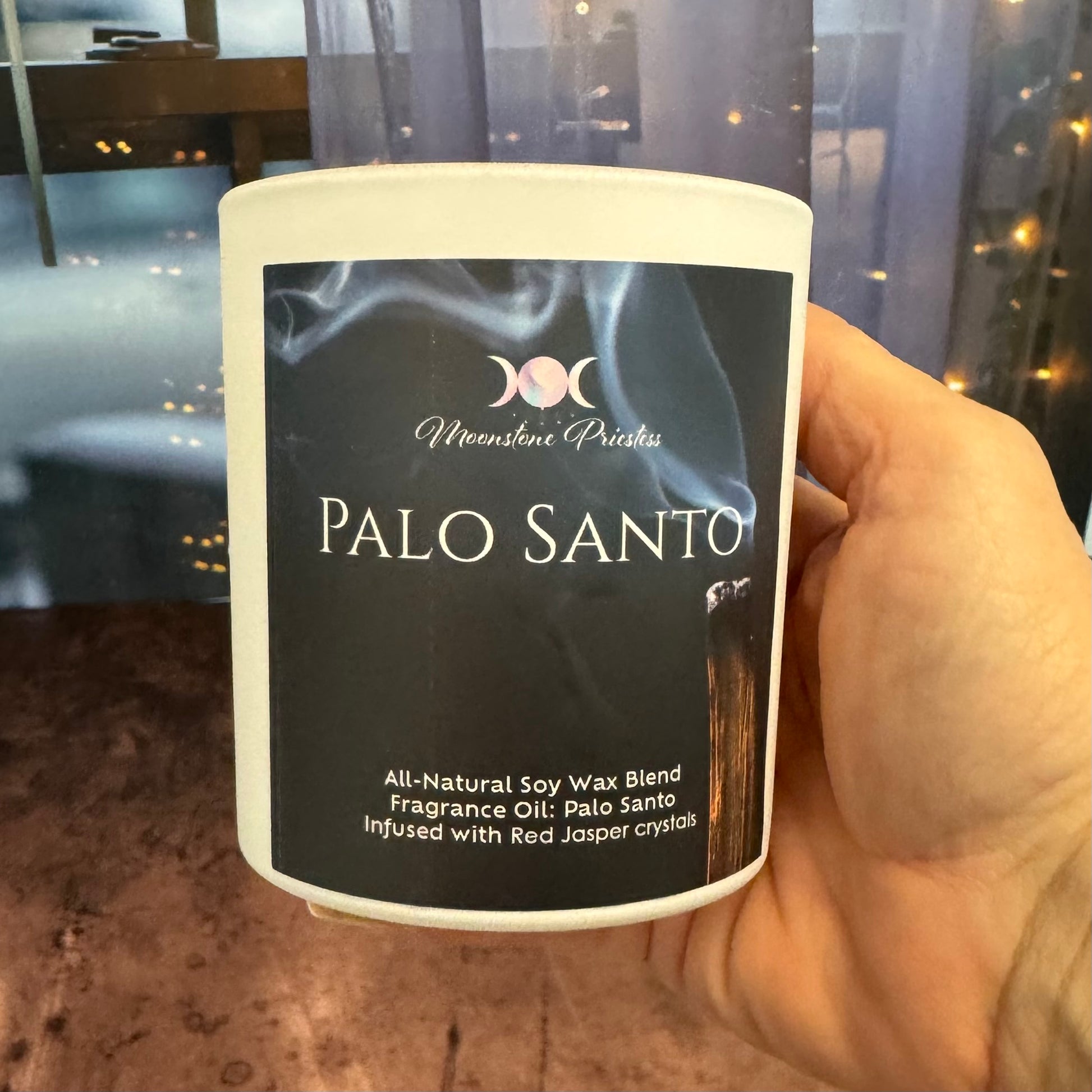 Candle labeled 'Palo Santo' held by a hand with a blurred background
