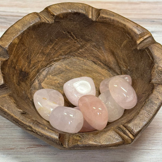 Wooden bowl with rose quartz stones on a light wooden surface