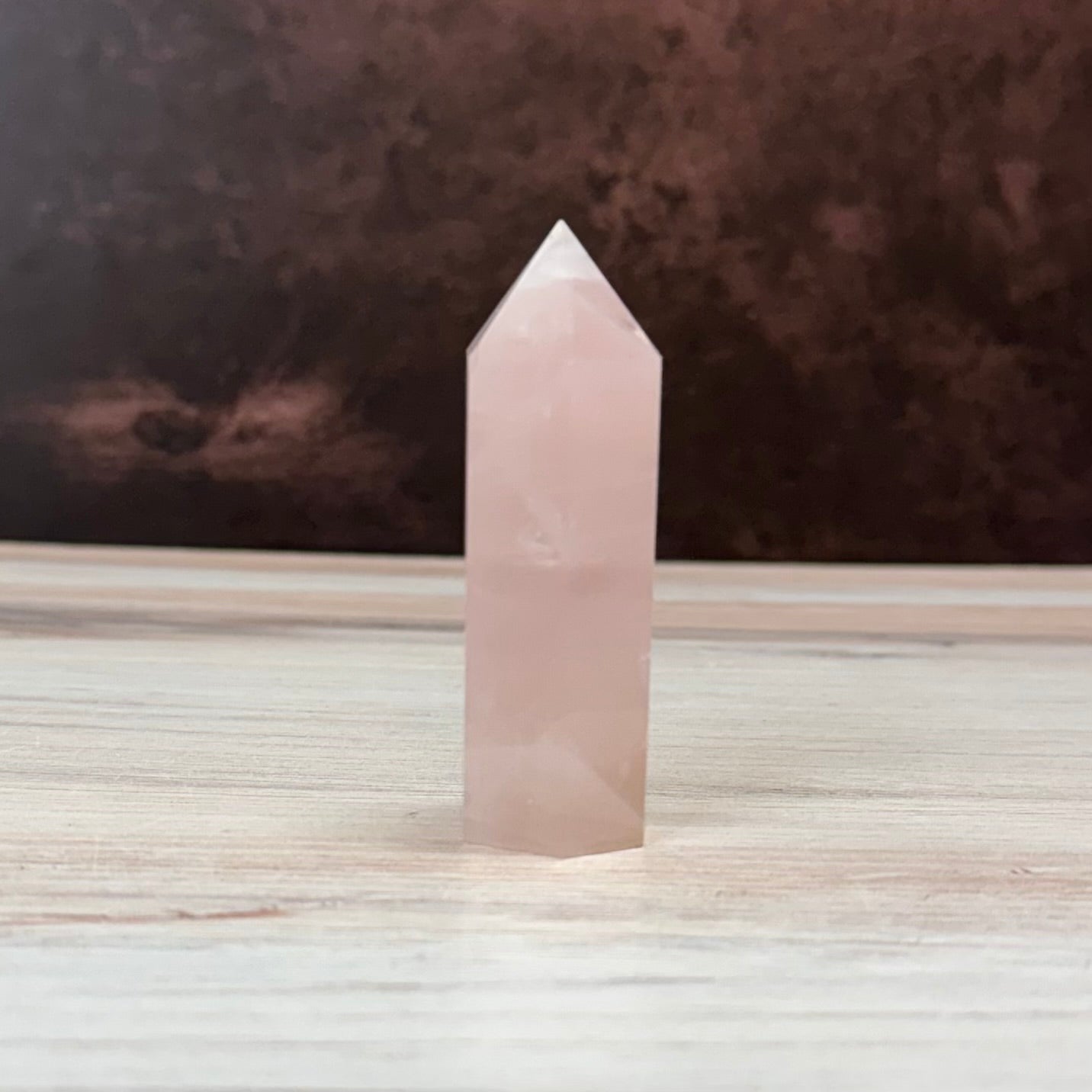 Rose quartz crystal tower on a wooden surface with a dark background