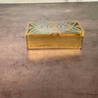 A gold-colored deck of cards with a decorative blue and gold celestial design on the top, resting on a gray concrete floor.