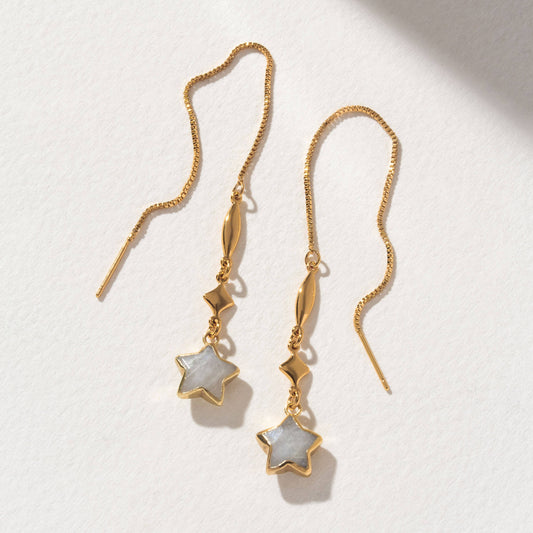 Gold earrings with star-shaped charms on a light background