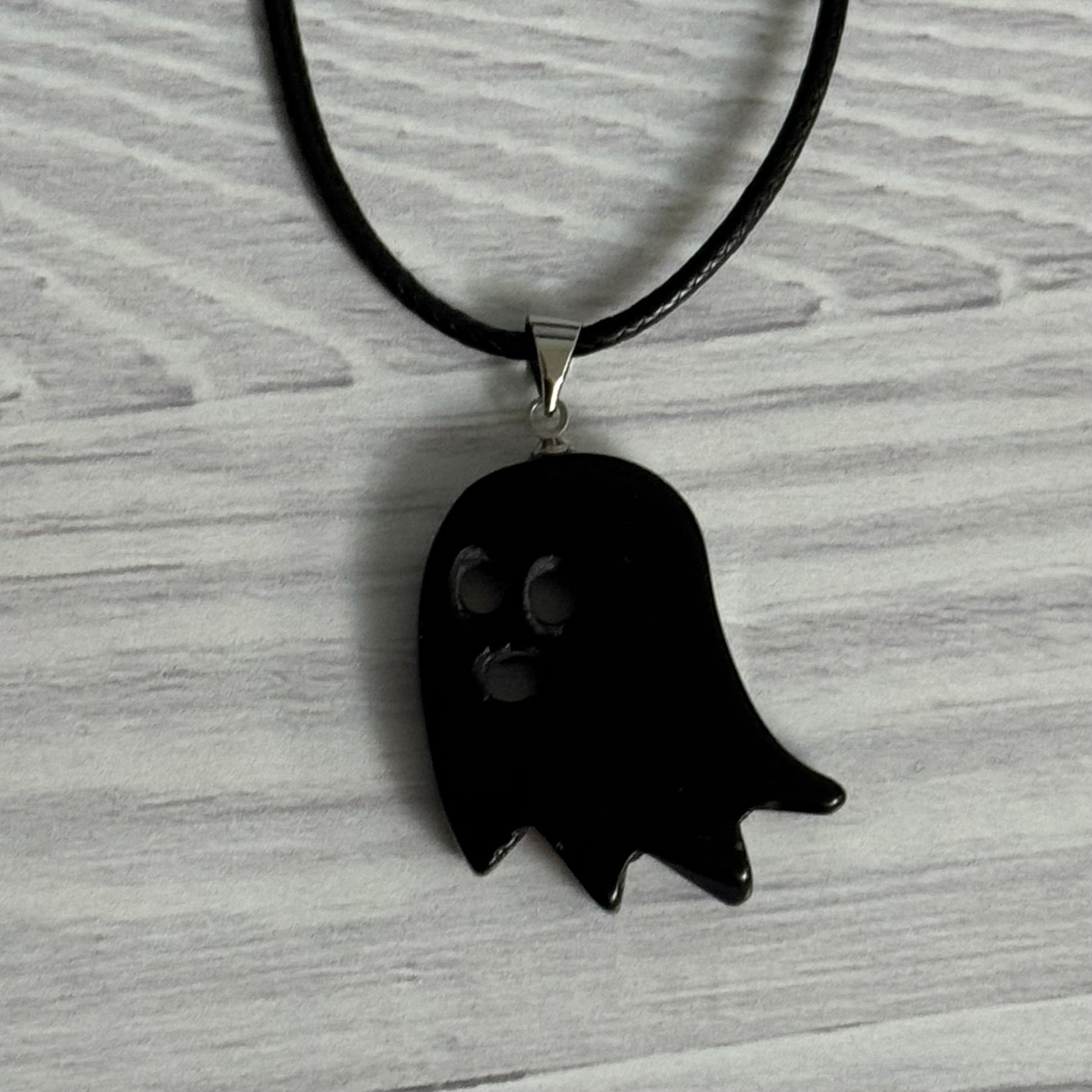 Black ghost-shaped pendant on a black cord against a gray background