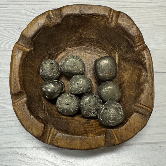 Wooden bowl with metallic stones on a light wooden surface