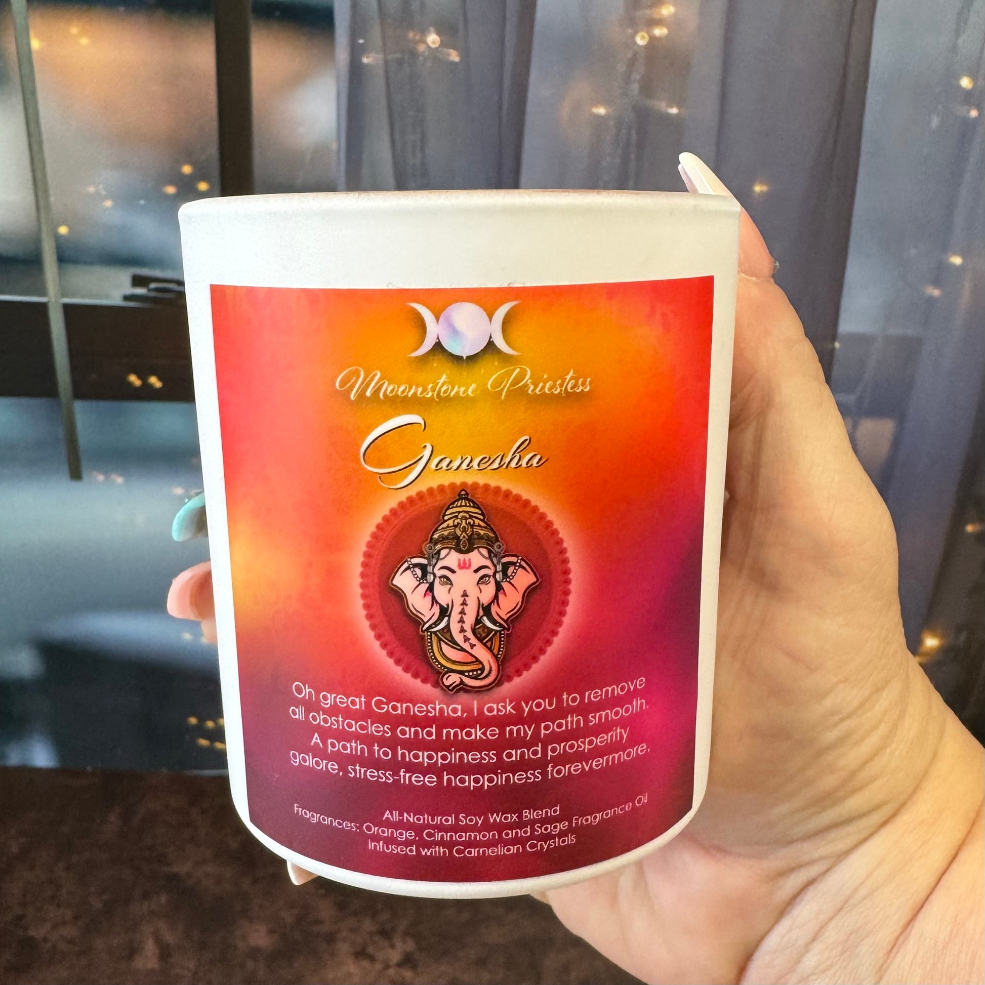 Candle with Ganesha design and text held by a hand against a blurred indoor background