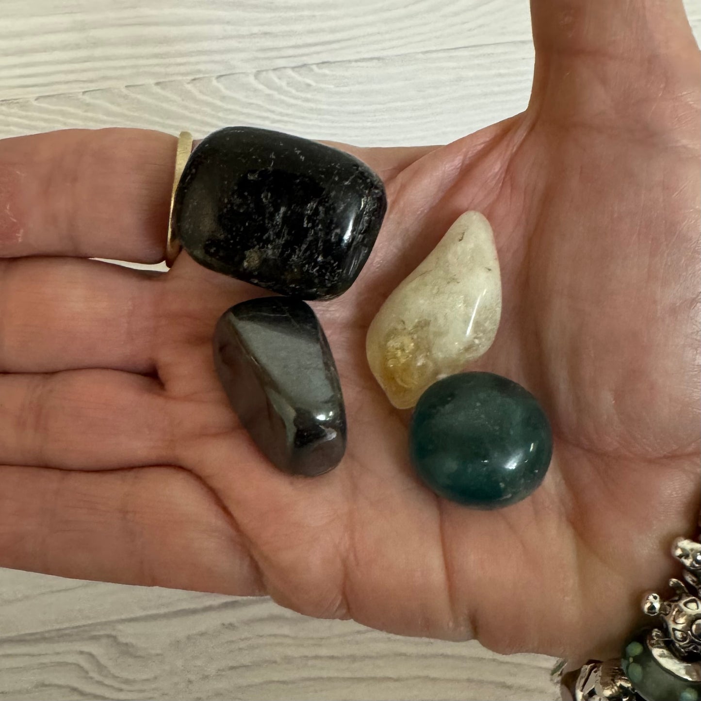 Hand holding four different stones on a light wooden surface