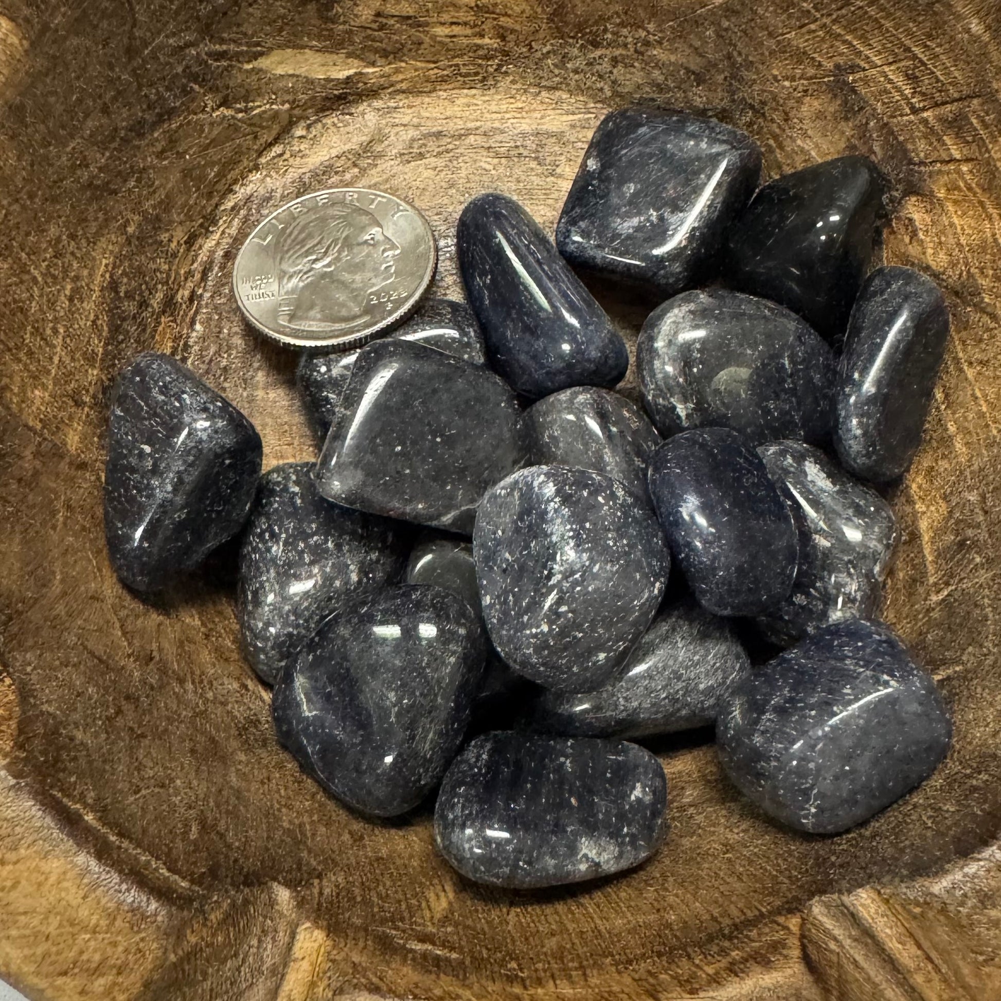 Tumbled black stones on a wooden surface with a quarter for scale
