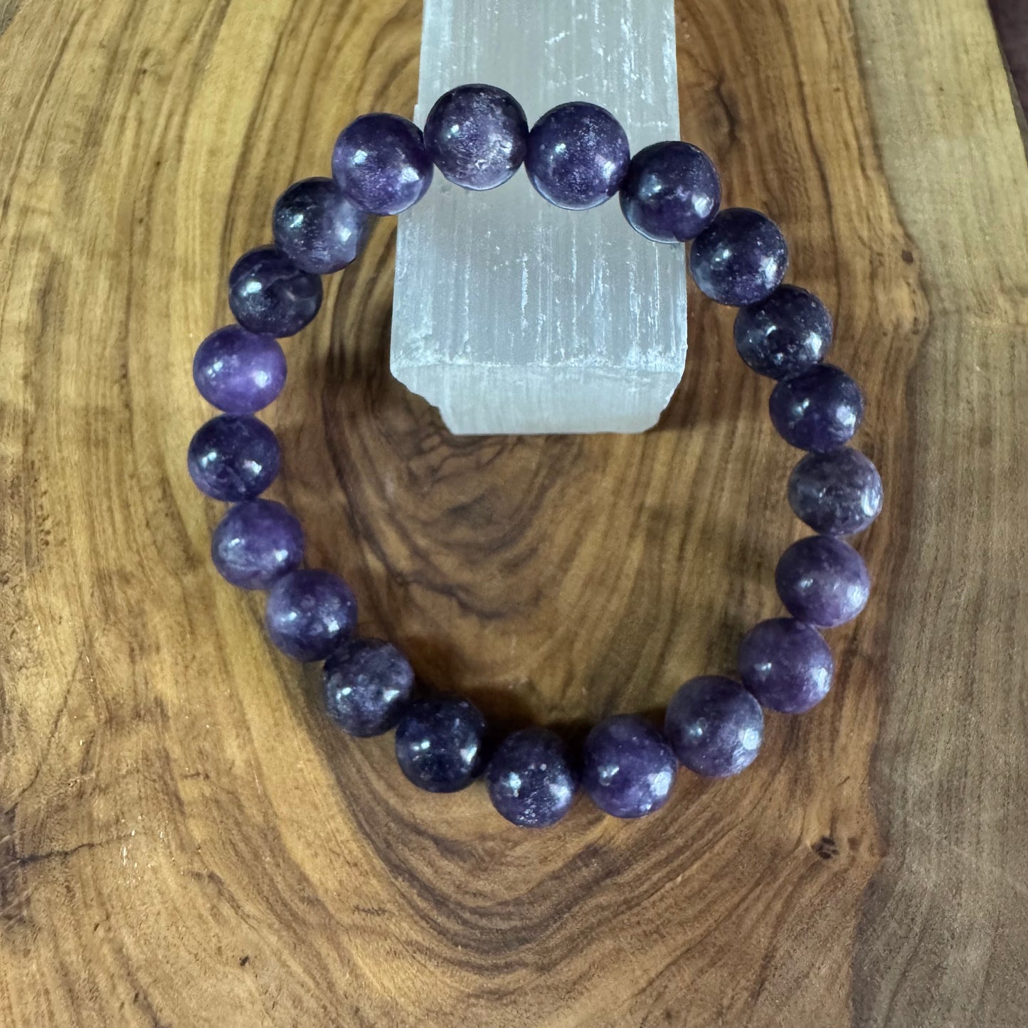 Purple beaded bracelet on a wooden surface with a crystal in the background