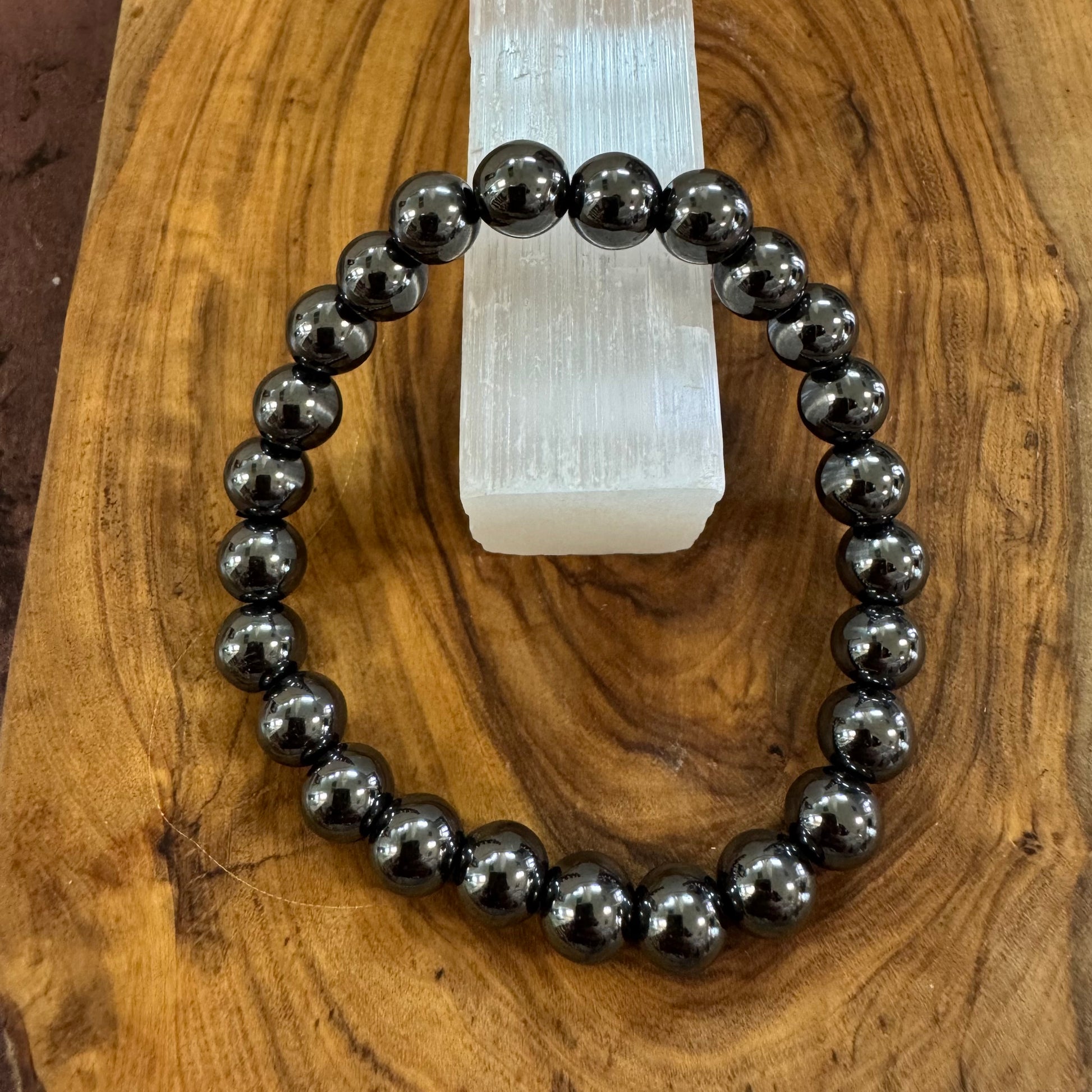 Black beaded bracelet on a wooden surface with a crystal in the background