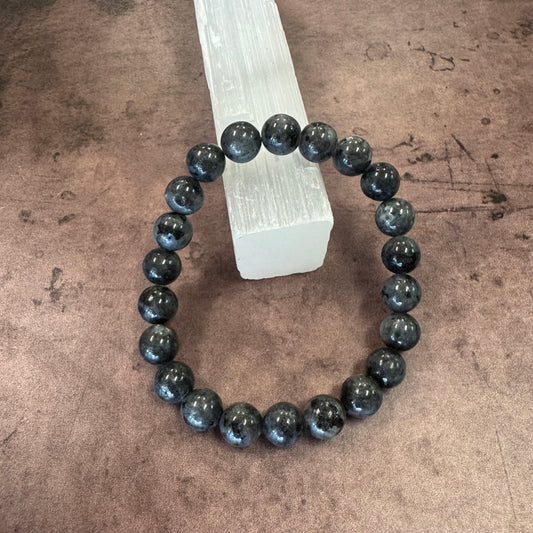 Black labradorite beaded bracelet on a wooden block against a brown background