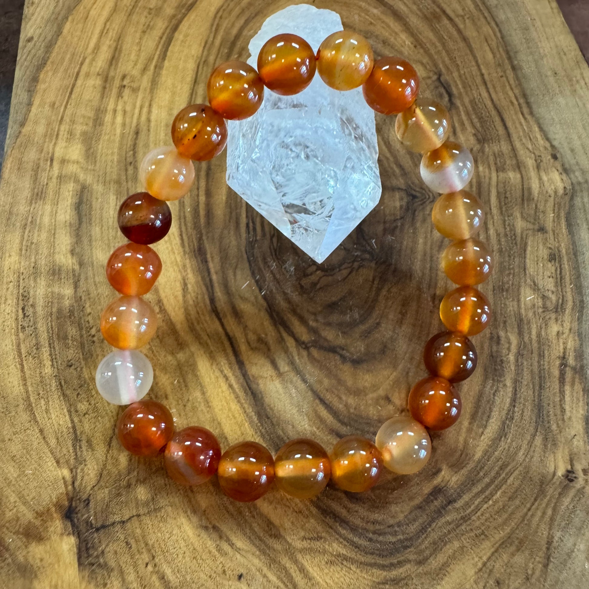 Beaded bracelet with orange and white beads on a wooden surface with a crystal.