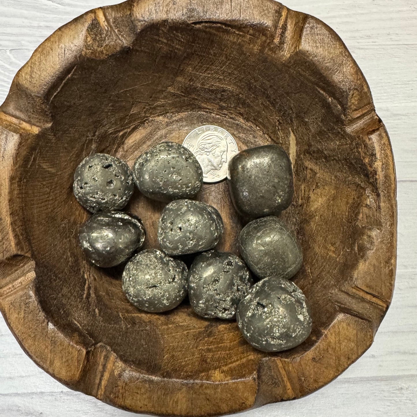 Wooden bowl with metallic stones and a coin on a light wooden surface