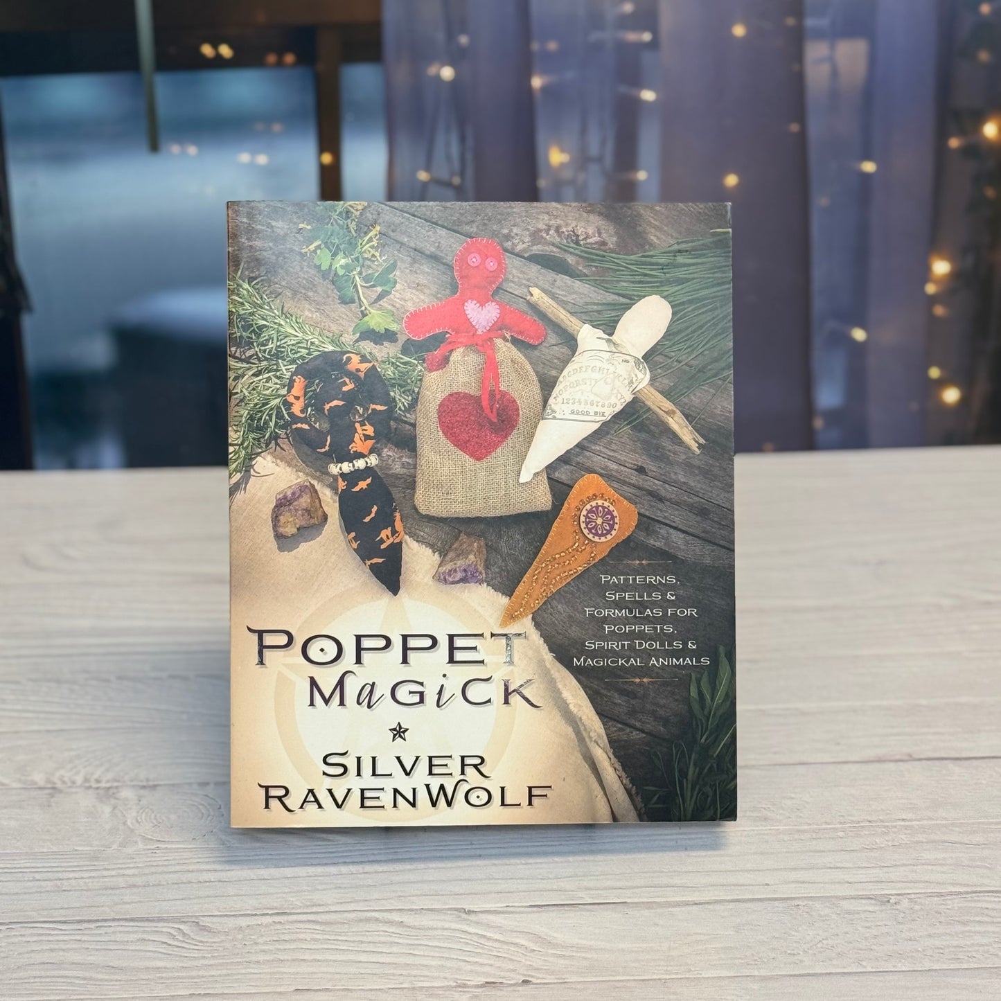 Book titled 'Poppet Magick' by Silver RavenWolf on a wooden surface with a blurred background.
