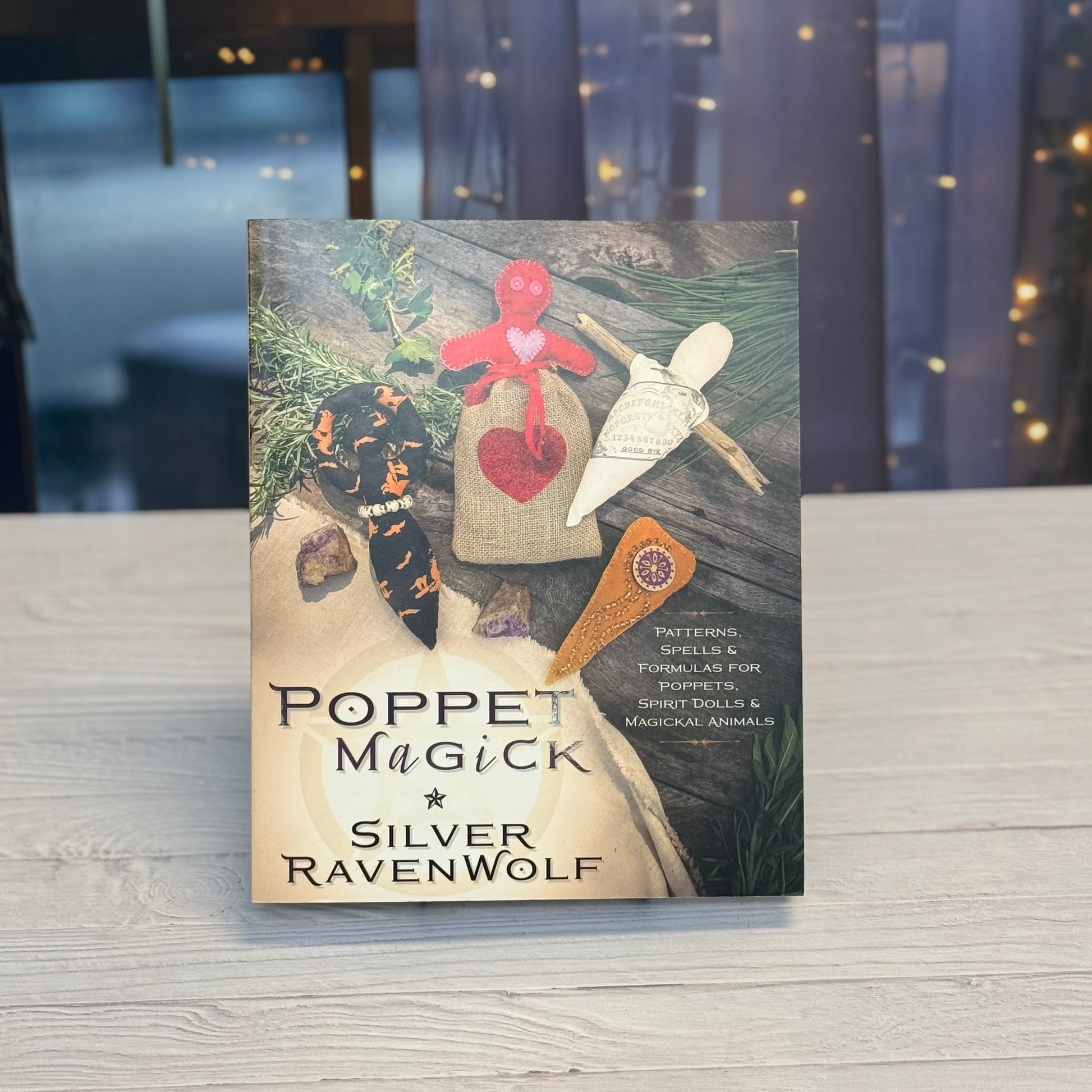 Book titled 'Poppet Magick' by Silver RavenWolf on a wooden surface with a blurred background.