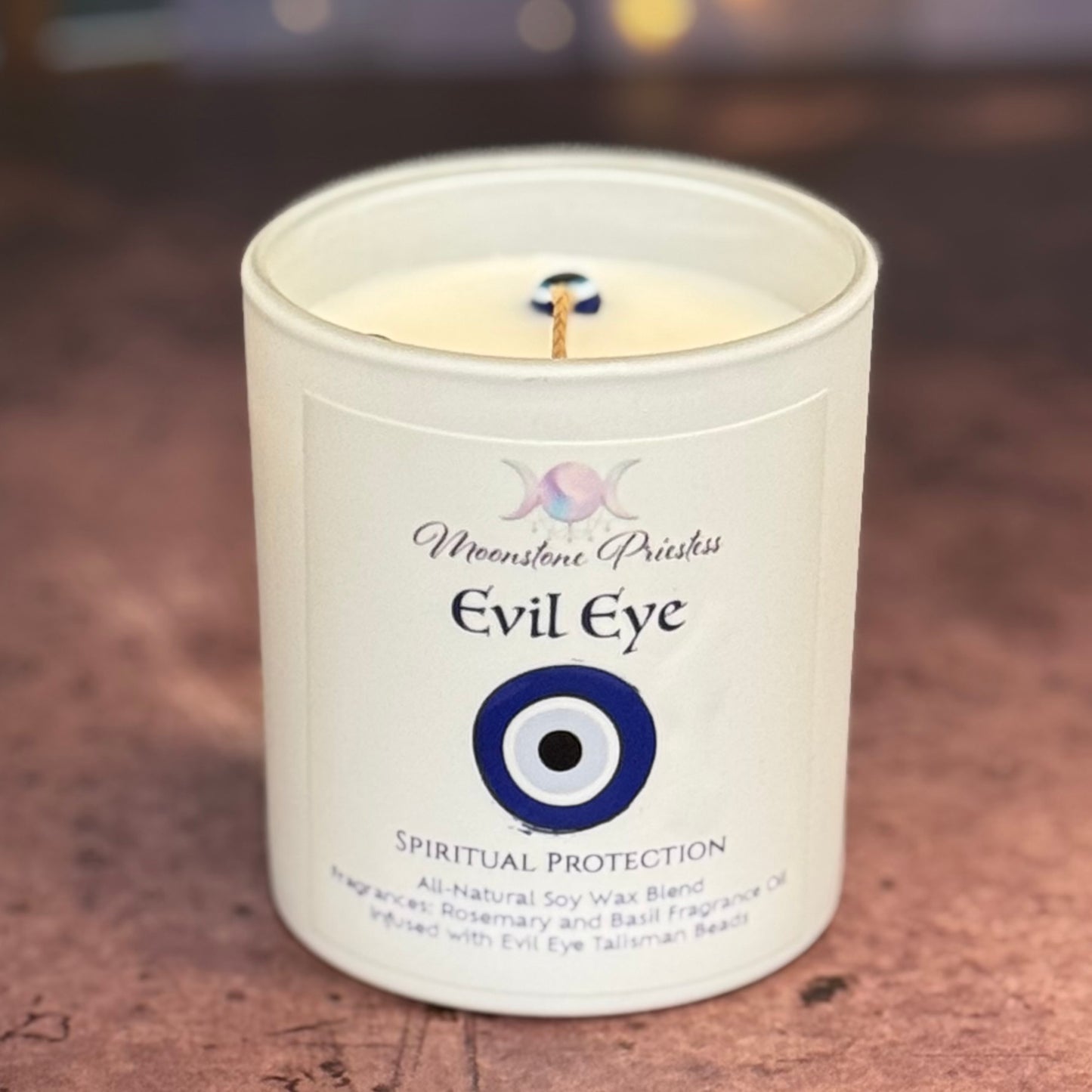 Candle in a white container with 'Evil Eye' design and text on a wooden surface.